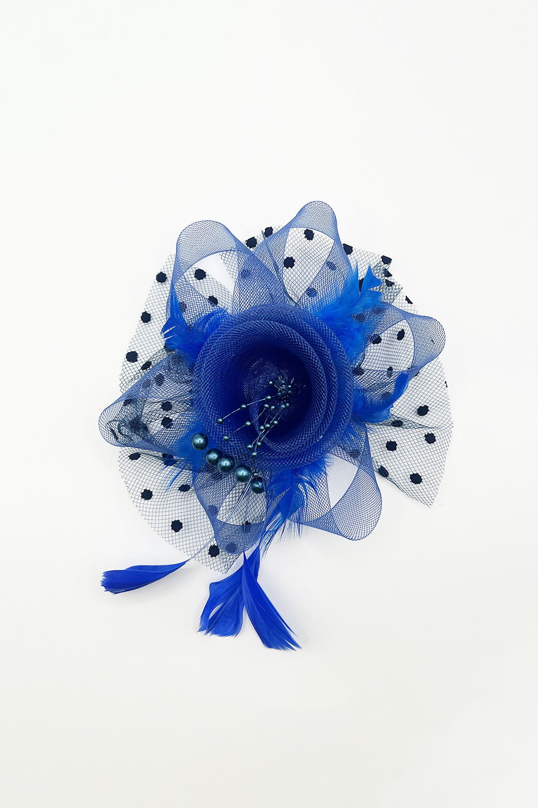 A royal blue fascinator hair accessory featuring a layered mesh flower, polka-dotted tulle, feathers, and tassels, photographed on a clean white background.