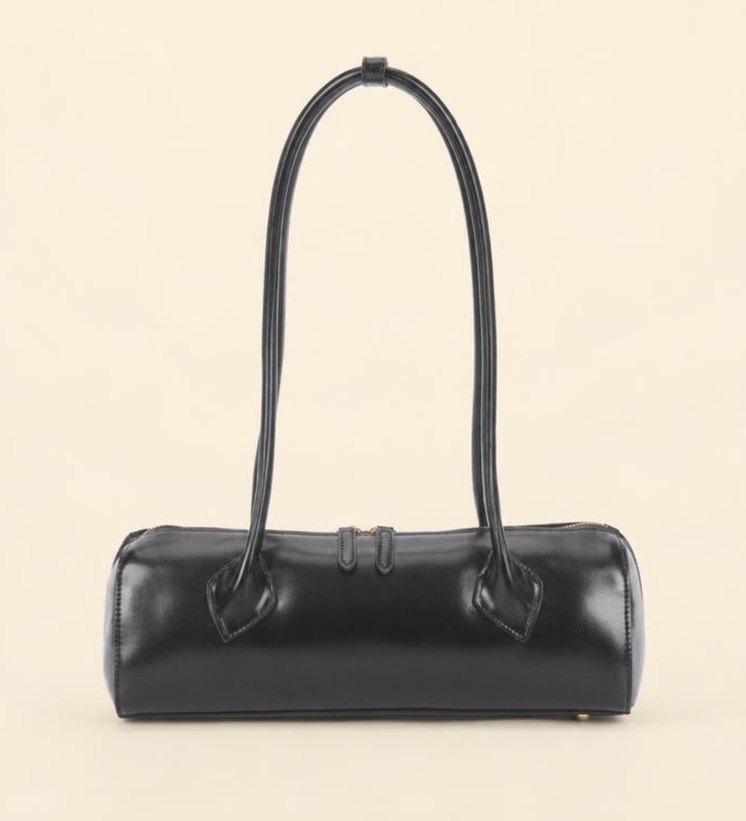 A black leather cylindrical handbag with a single top handle, photographed against a solid light beige background.