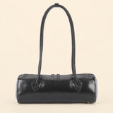 A black leather cylindrical handbag with a single top handle, photographed against a solid light beige background.