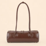 A dark brown leather cylindrical handbag with a single shoulder strap, photographed against a solid light beige background.